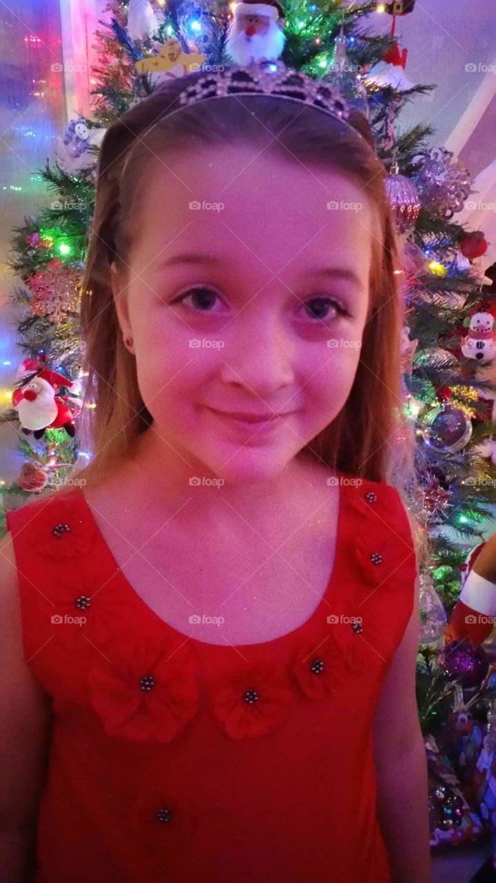 child looking and smiling wearing  a red dress while standing in front of her family Christmas