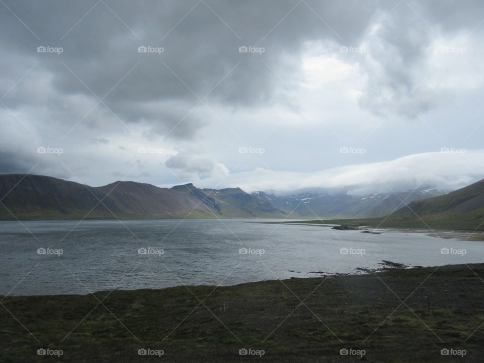 Moody Icelandic sky with volcano in the background, lake, and mossy lava field in the foreground 