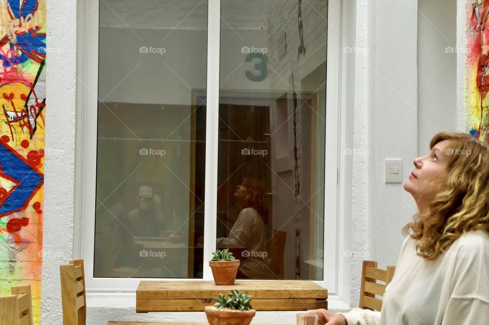 A beautiful woman looks up while her reflection is captured in a window.