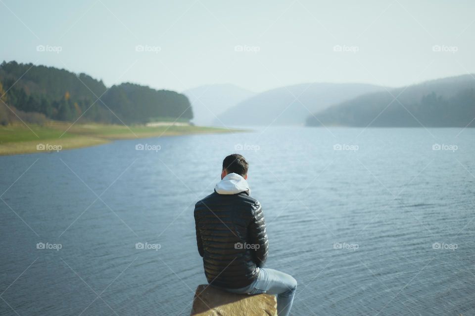 Man sitting on rock at the lake .