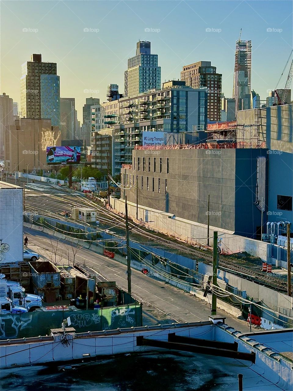 From the staircase of the “Pulaski Bridge” at “Newtown Creek” in LIC we overlook the tracks of the “Long Island Railroad” and a rectangle building housing “iFly”, an indoor flight simulator mimicking parachuting free fall. 2024. Hypnotic Productions