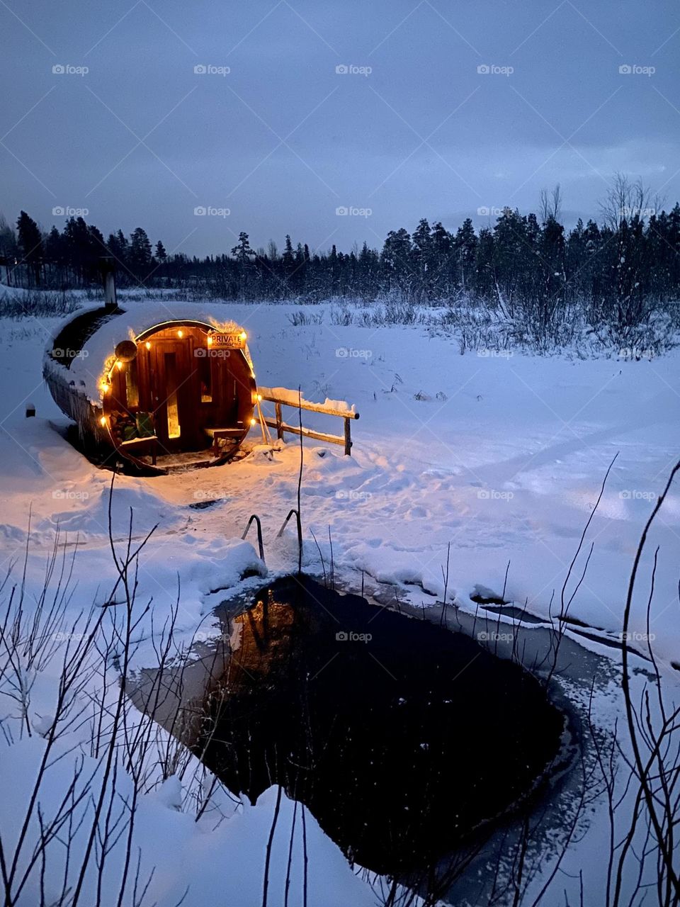 Ice pool of the frozen lake outside of wooden sauna decorated with Christmas lights