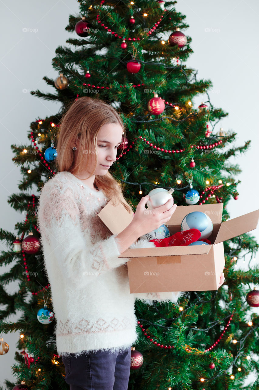 A teenager holding ornament in front of Christmas tree