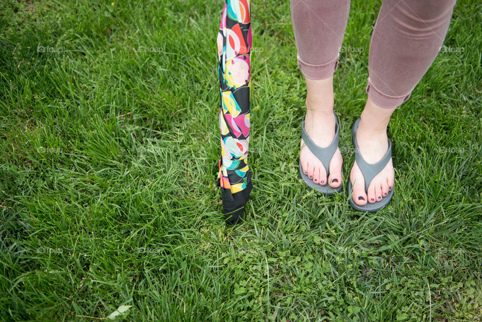 Close-up of a standing woman's flip flop sandals and umbrella outdoors