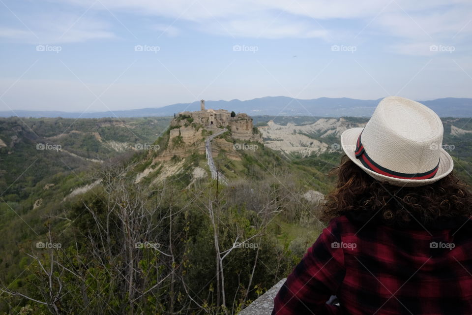 Woman with hat looks at the ancient Civita di Bagnoregio from afar