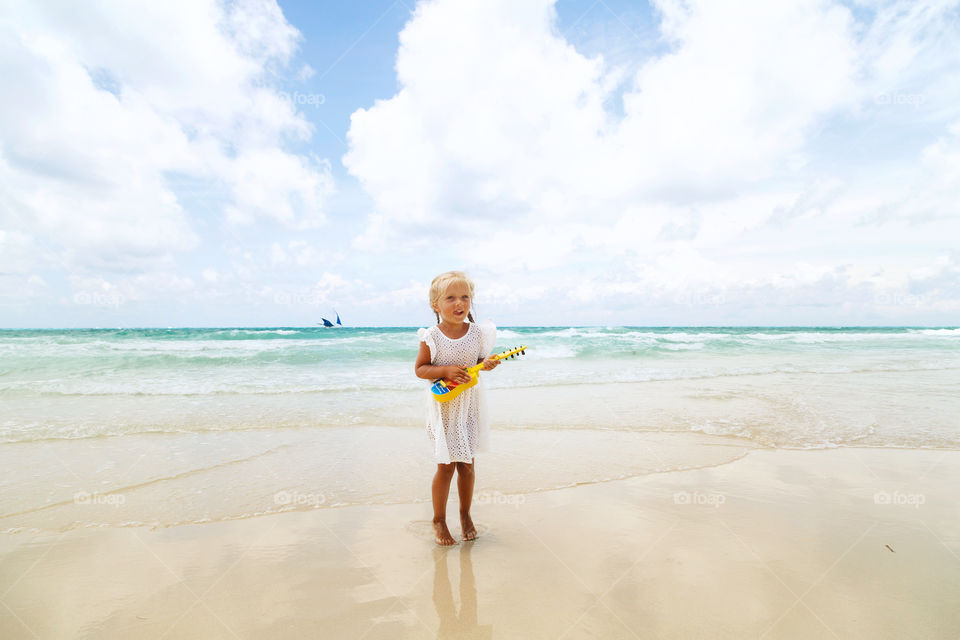 Cute little girl with guitar on the beach 