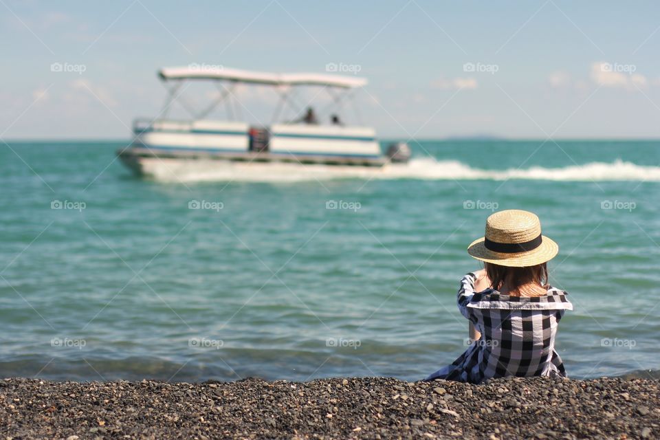Little girl sits on the shore and looks at a pleasure boat
