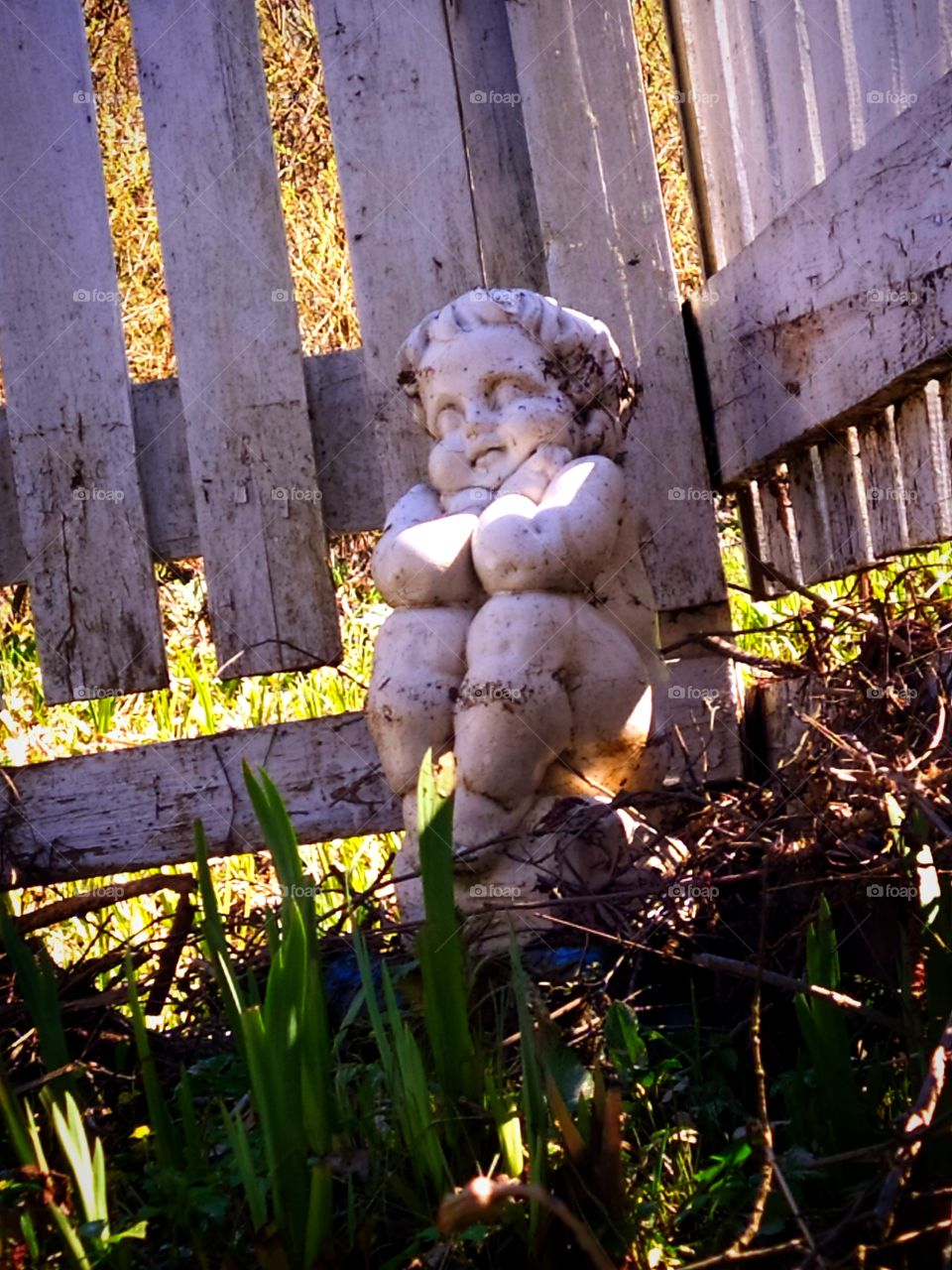 Clay sculpture of a seated cupid by a wooden fence