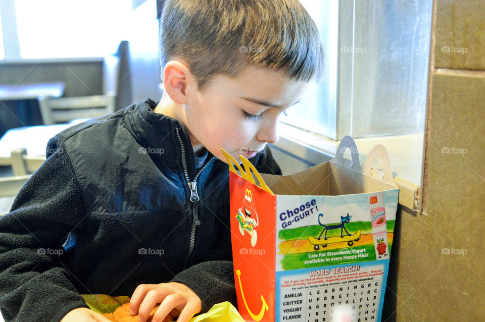 Young boy looking curiously into a McDonald's happy meal box while sitting in a McDonald's restaurant