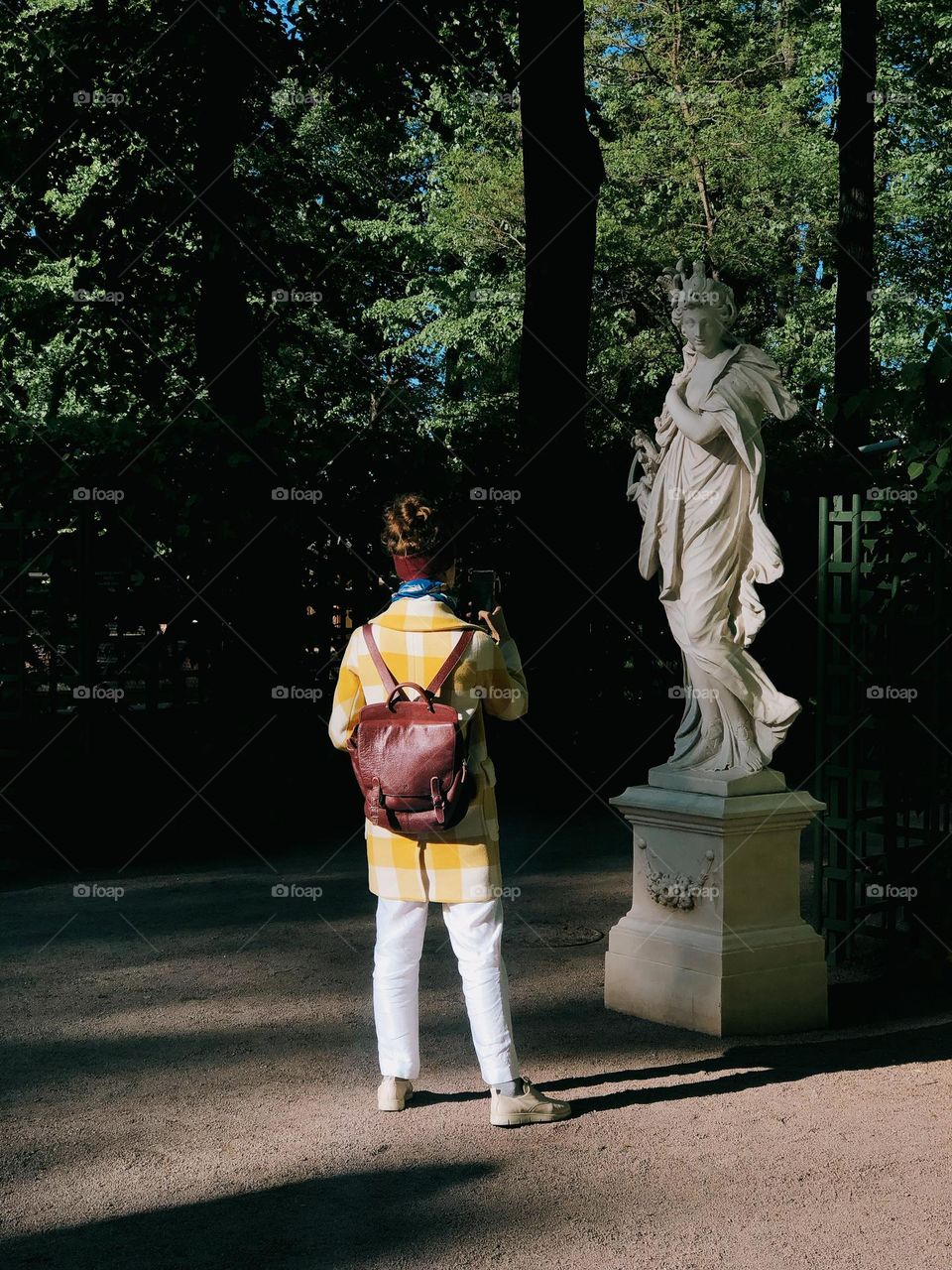 Young unrecognisable woman taking photo in summer garden on a sunny day, back view