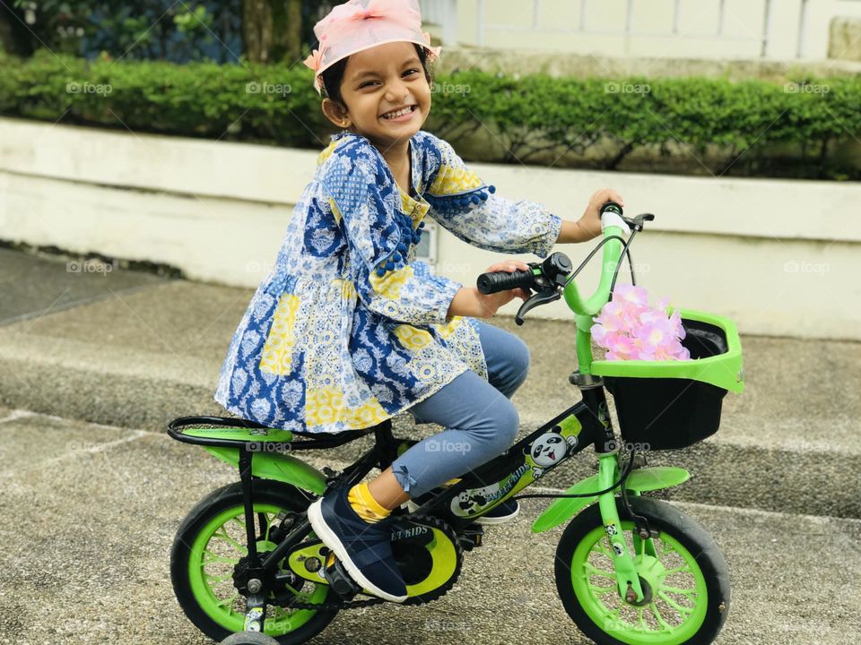 A baby girl on green bicycle in her way on road and she smiles adorable 🥰