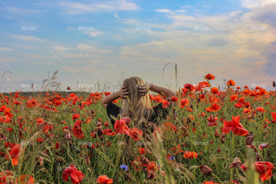 The girl is standing on the poppy field.