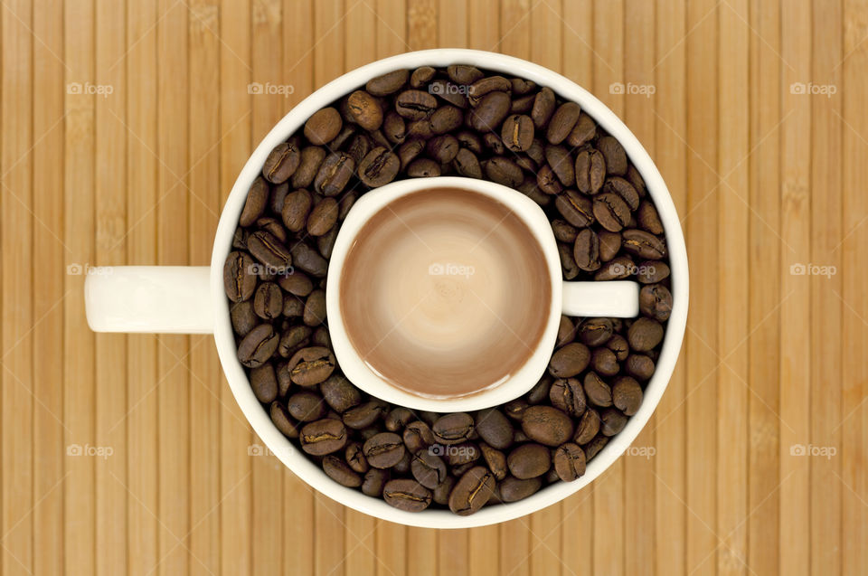 Small cup with coffee placed in to bigger cup with coffee beans