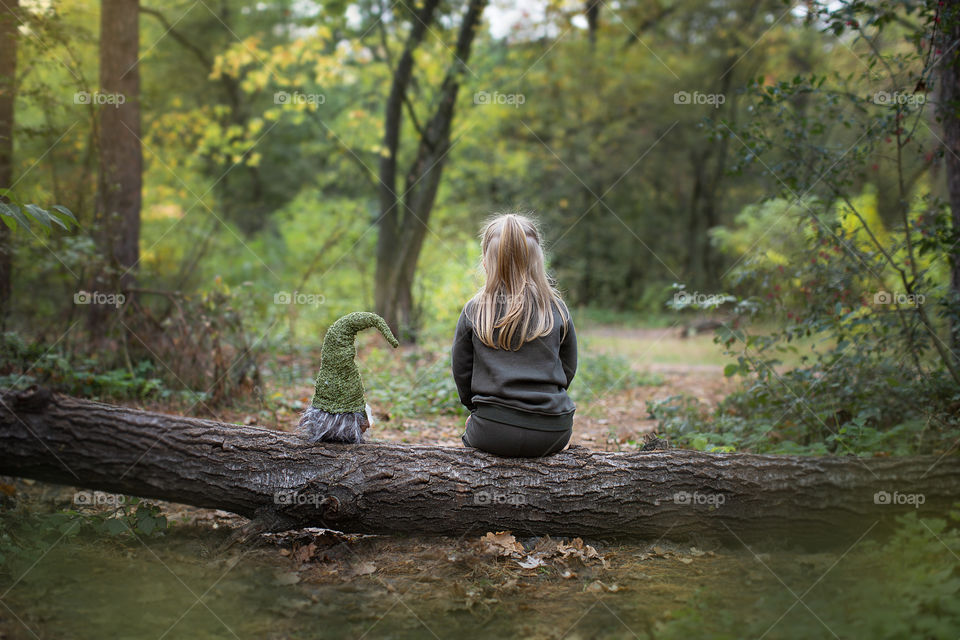 a girl and a gnome are sitting in the woods on a stump