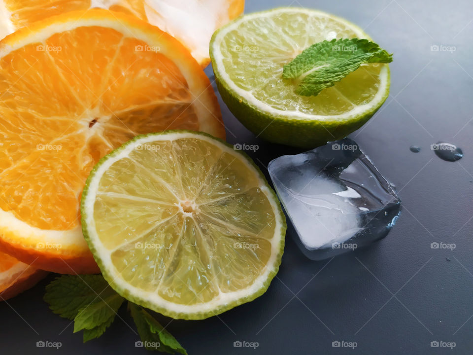 Slices of orange and lime with pieces of ice on dark