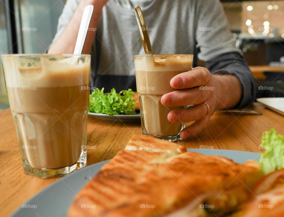 Person with cold coffee and bread on table