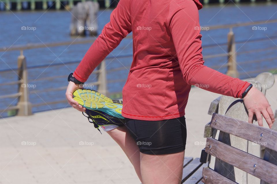 Female runner outside stretching leg muscles for a run along the Hudson River in Manhattan, New York City.