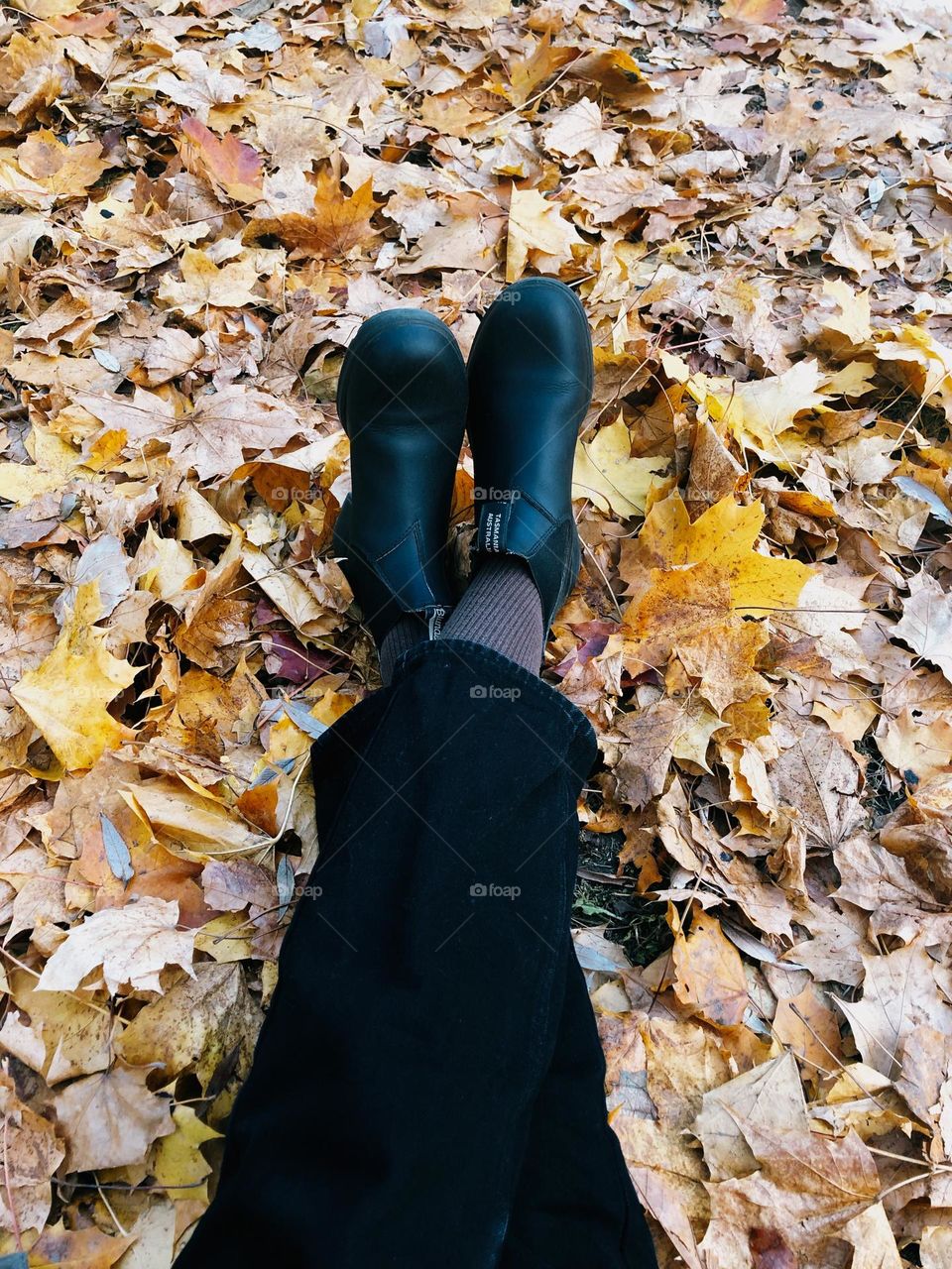 Unrecognisable woman lies on the yellow autumn leaves in the garden 