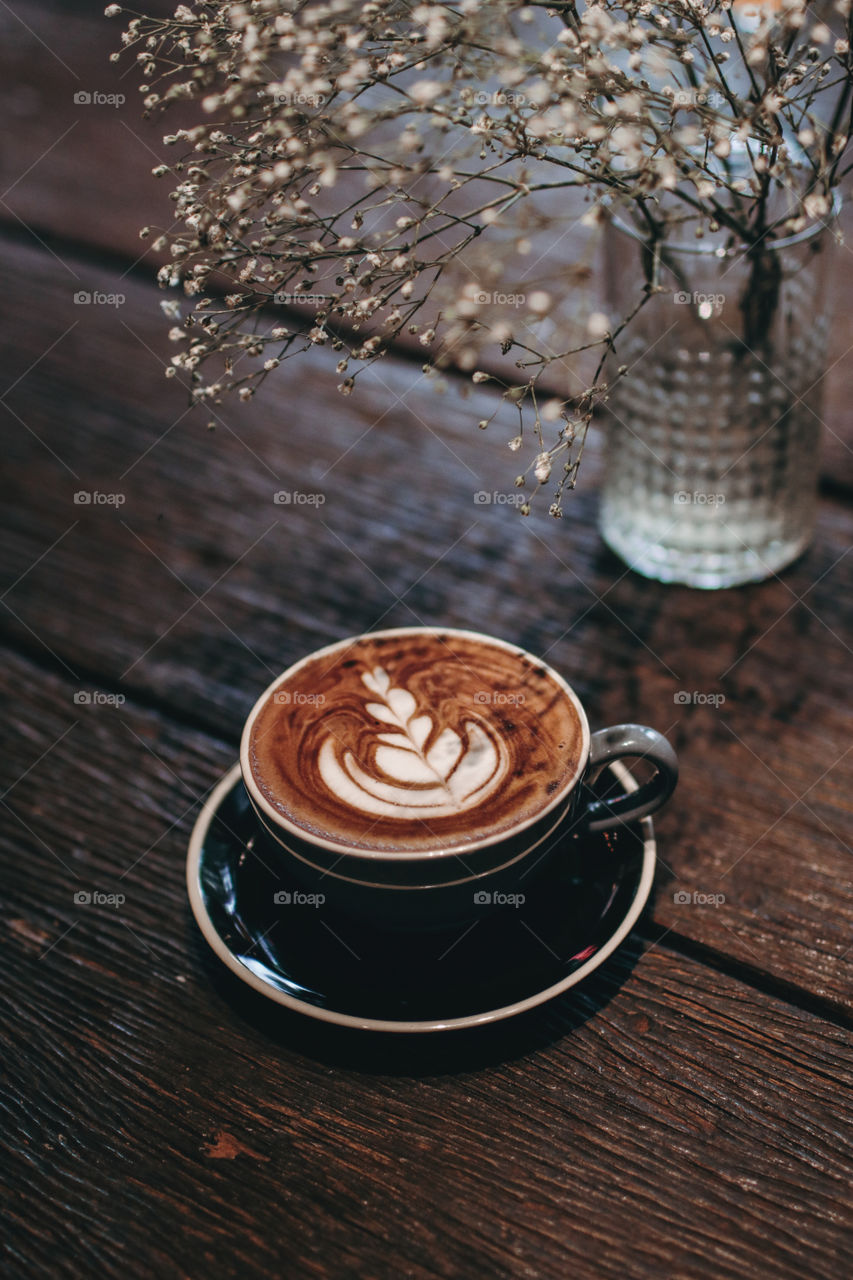 Hot coffee latte on wooden table near white flower