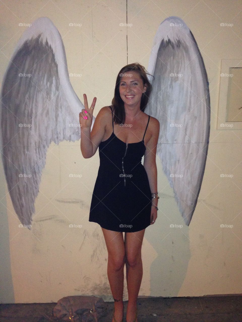 Woman gesturing v sign in front of wings painted on wall