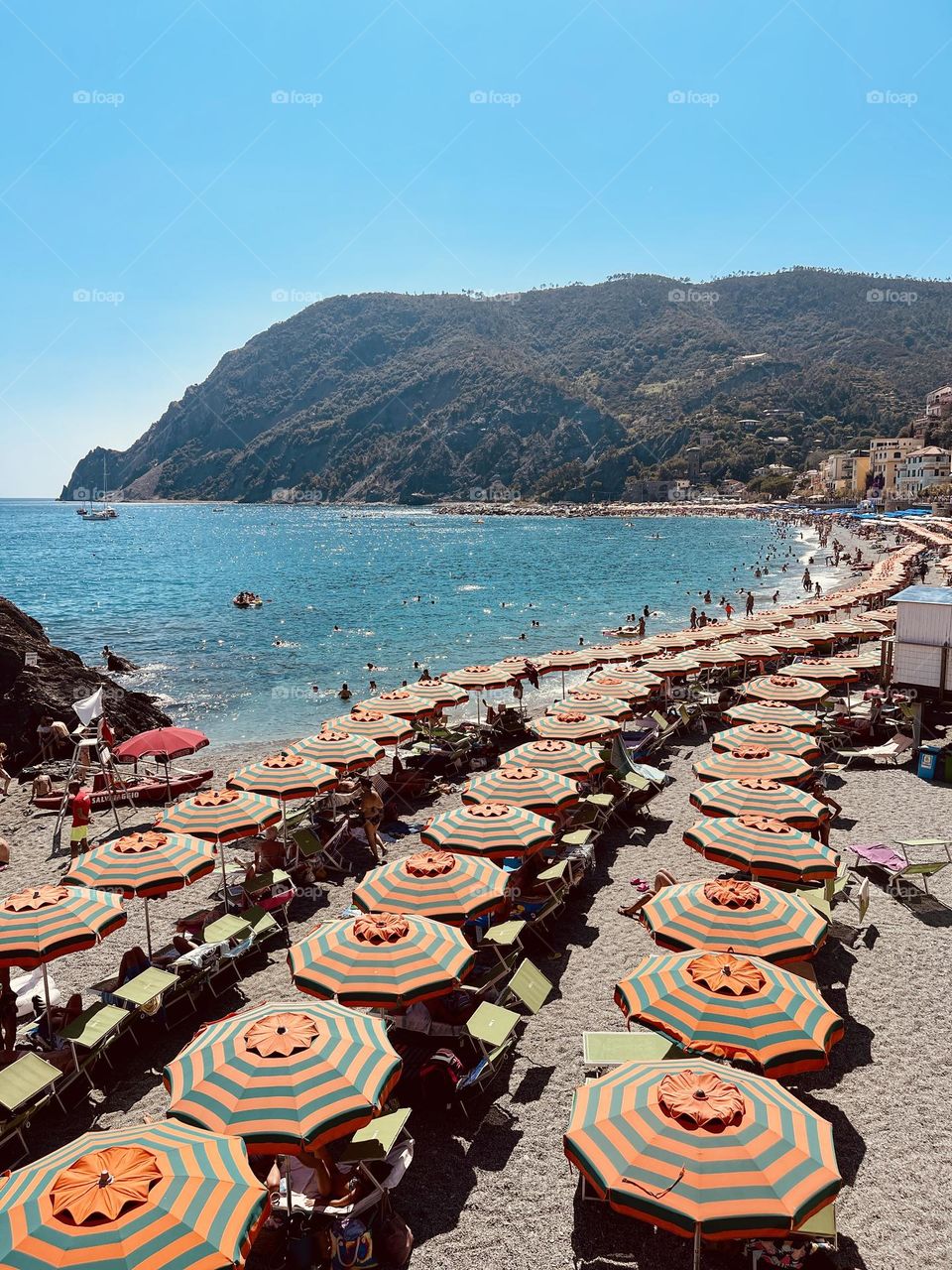 Beautiful beach lined with blue and orange umbrellas and a lush green mountain side