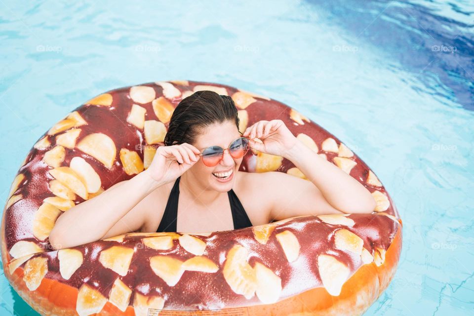 Happy young woman plus size body positive in inflatable doughnut circle swimming in the pool, summer vacations