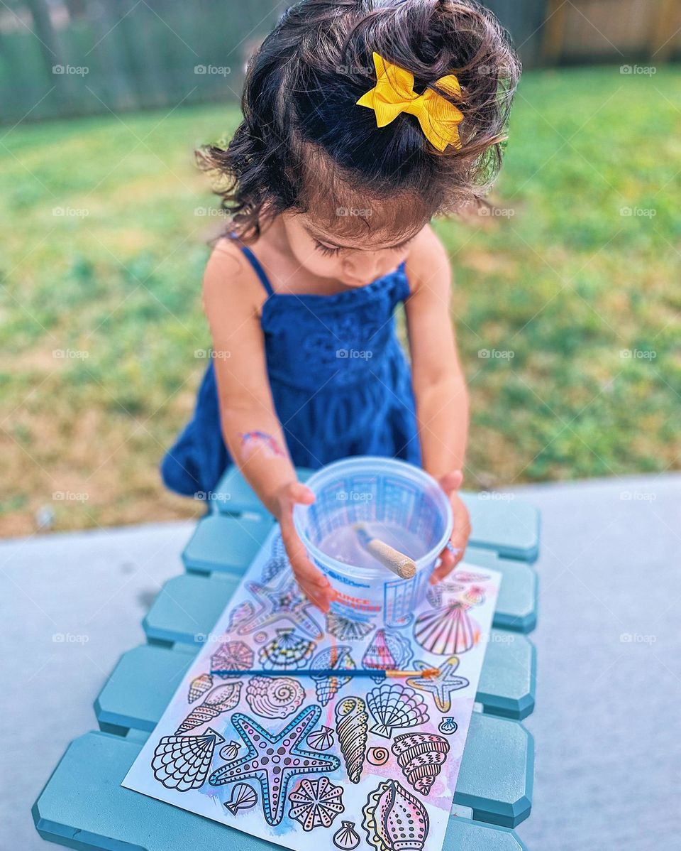 Little girl painting outside, toddler holding paint bucket, toddler painting seashells, little artist outside, summertime activities 