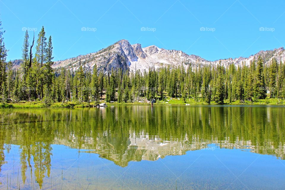 Beautiful reflection of a high mountain lake in the backcountry of Idaho with fly fisherman in the background. 