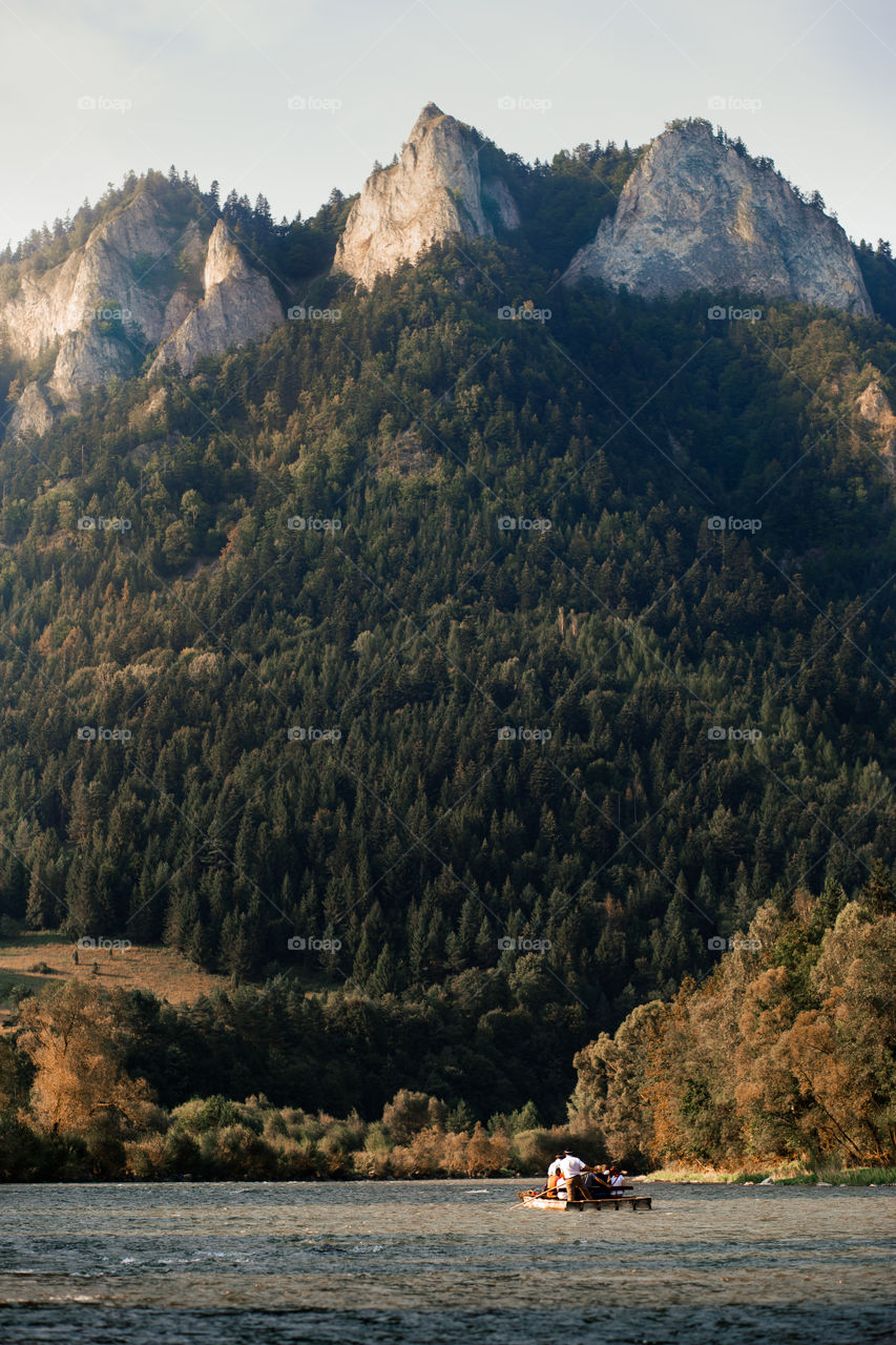 Raft ride on The Dunajec river at the foot of Pieniny Mountains. Group of people enjoying trip on raft going down the river. Trzy Korony (Three Crowns) peak over the river