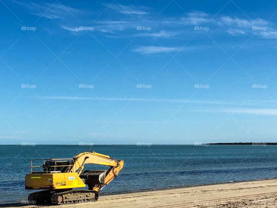 Yellow excavator heavy machinery traveling along south Australian beach 