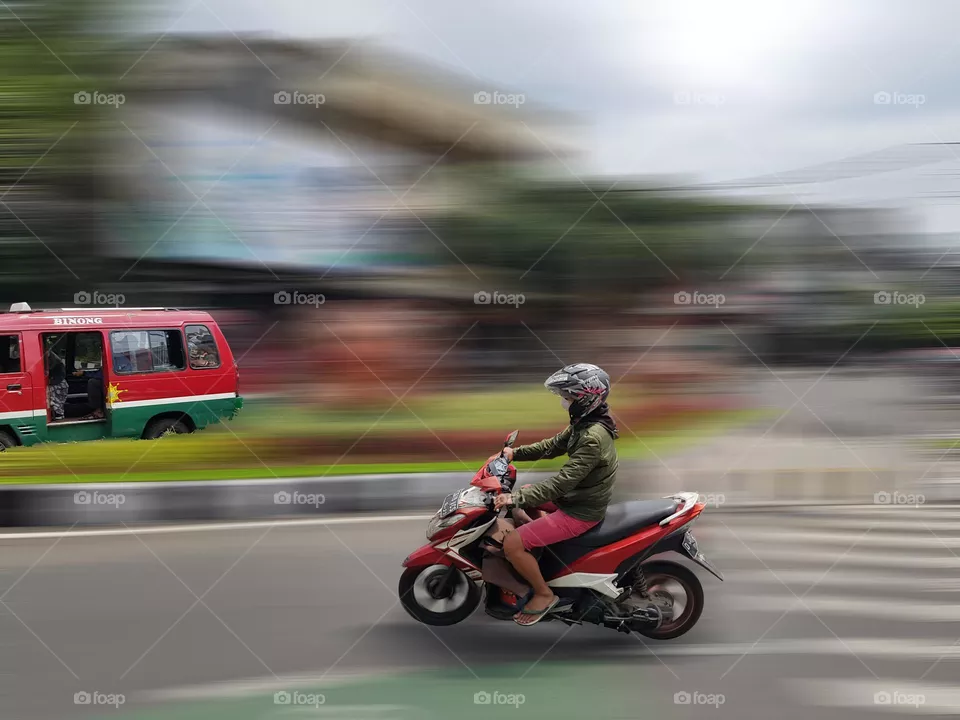 Riding motorcycle on the road, the type of two-wheeled transportation vehicle, fuel is gasolin, fuel -efficient vehicle, much liked by general public, on the main street on the citu of bandung, indonesia, the color is red,