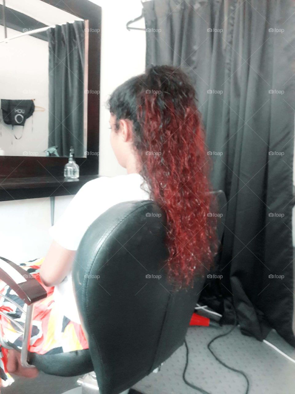 a girl with coloured curly hair.sitting on a chair in saloon