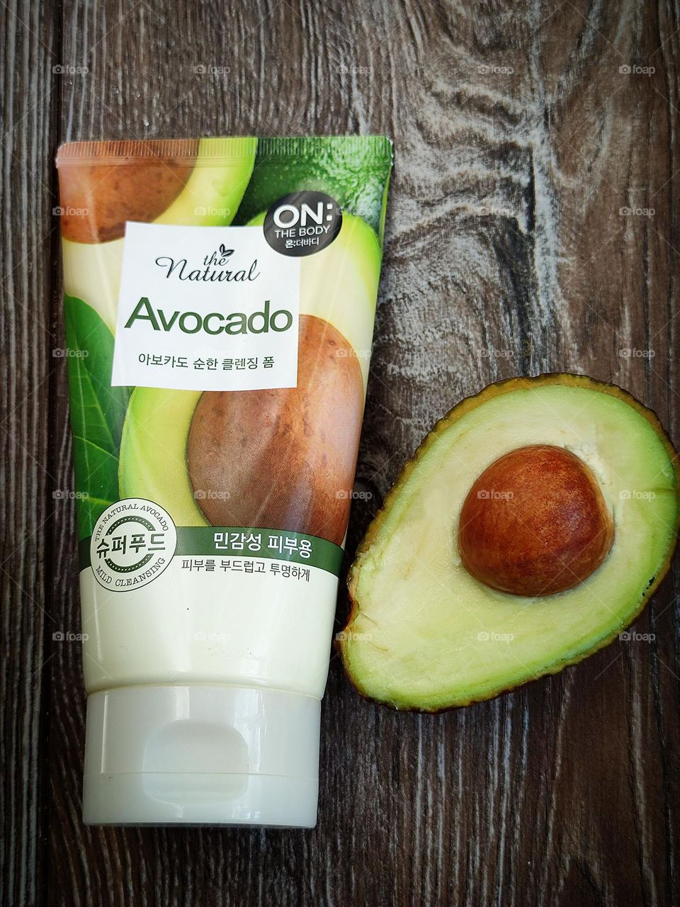 Tube of facial wash "On the body Natural Avocado", with avocado oil and fruit extracts (Korea) and half avocado "Hass" on a wooden background