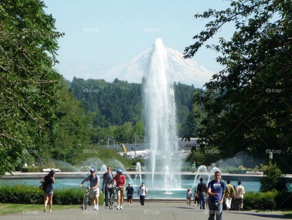 A fountain flows near Washington University with Mount Baker in the distance as individuals pass by on their way to classes