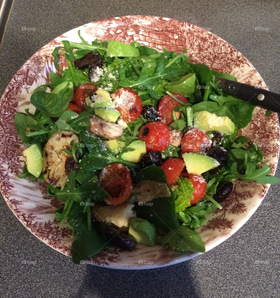 A fresh healthy salad of avocado and arugula with chargrilled cherry tomatoes and globe artichokes, finished with a sprinkle of Parmesan cheese. 