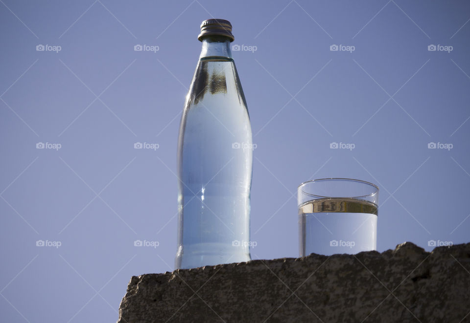 bottle and glass with cold fresh water against the sky