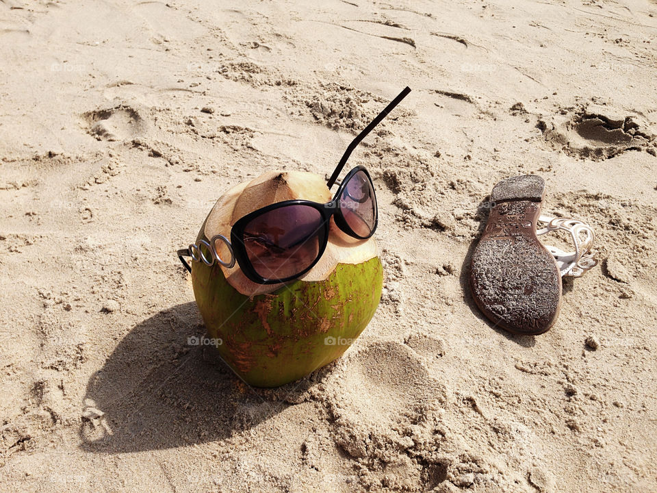 Coconut cocktail with sunglasses and beach slipper on sandy beach 