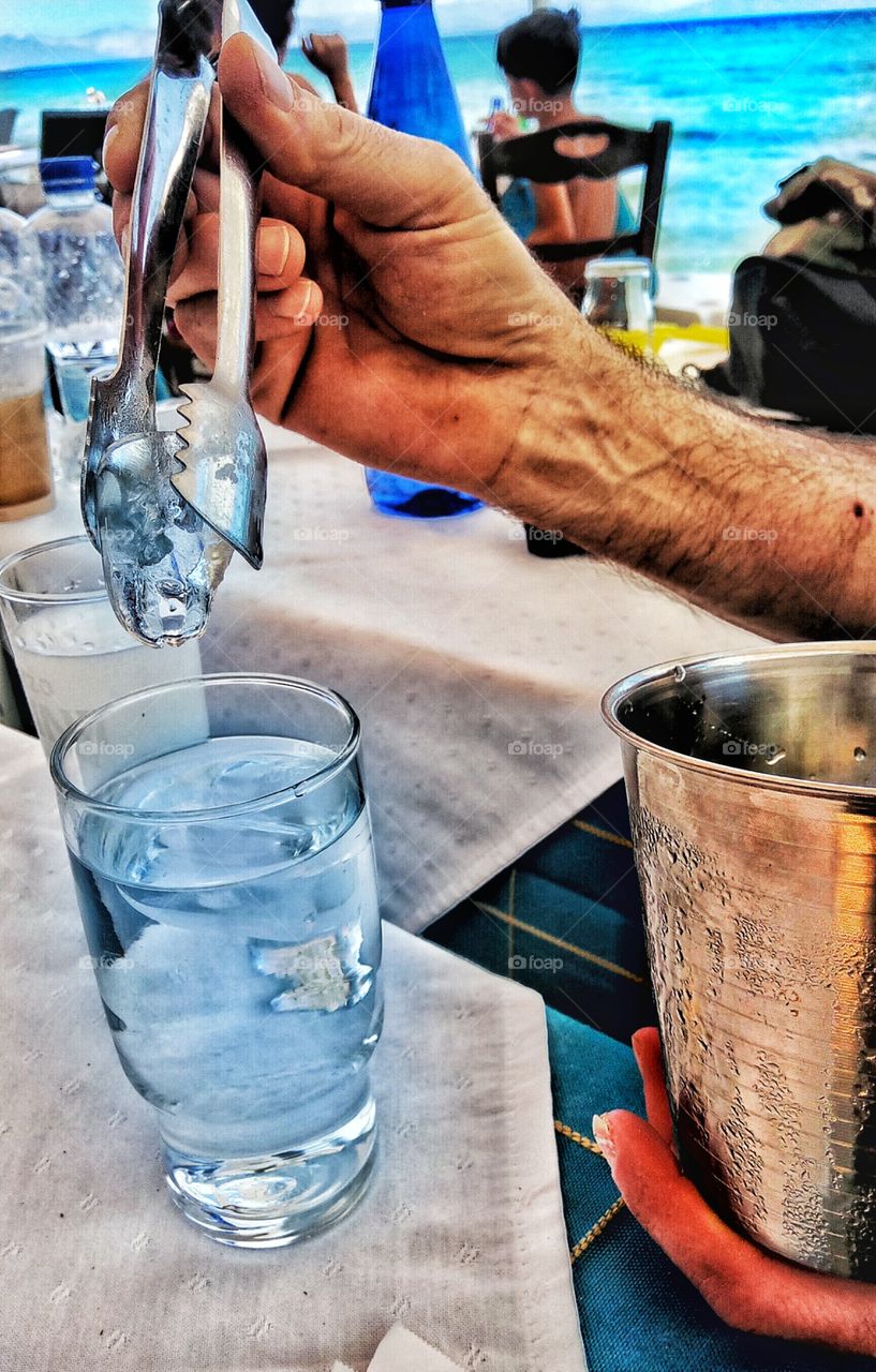 Putting ice in a drink in a restaurant by the sea...Artemida,Greece