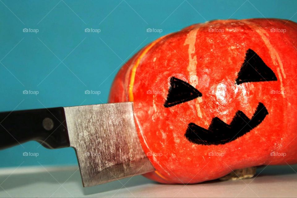 An orange pumpkin with a painted face is divided by a kitchen knife against a blue background