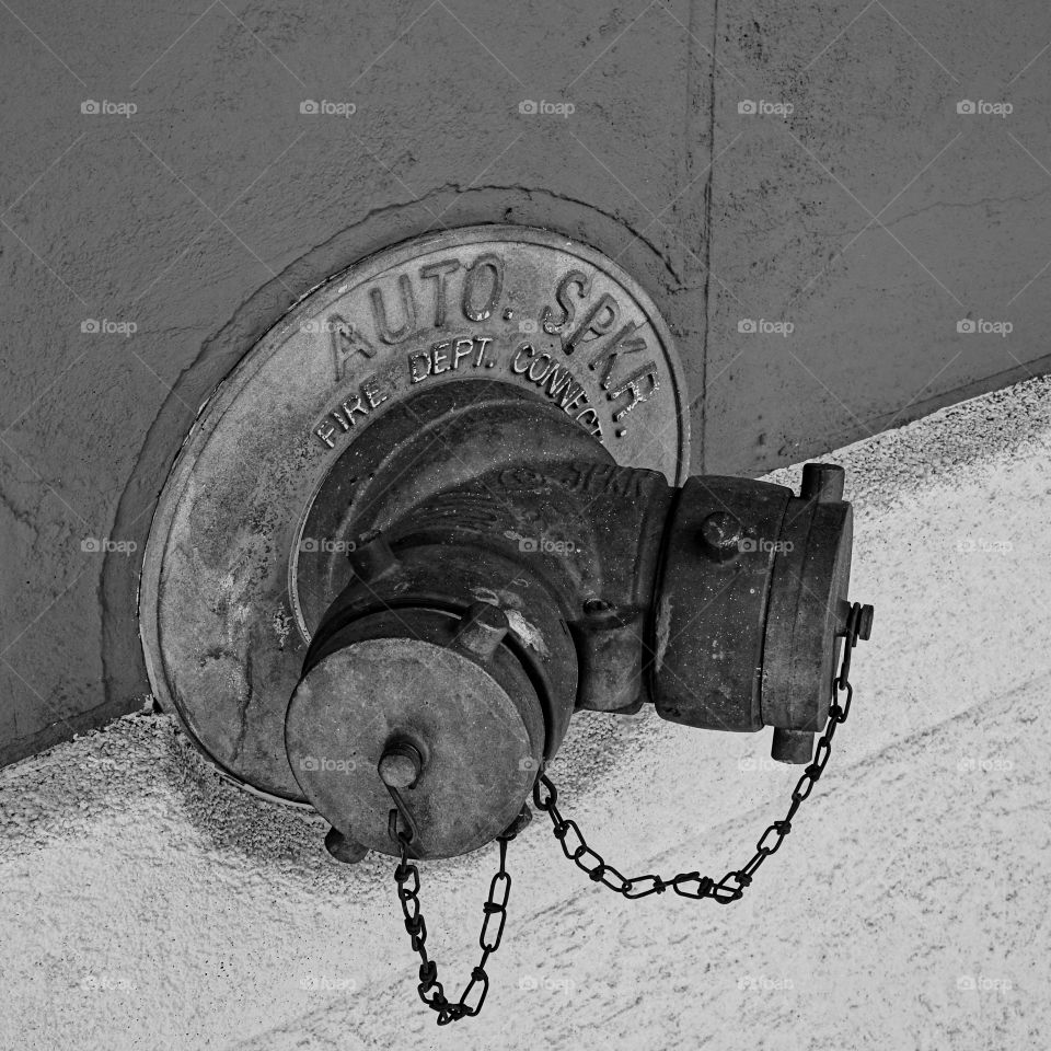 A double fire hose spicket hangs from the side of an old building downtown. 