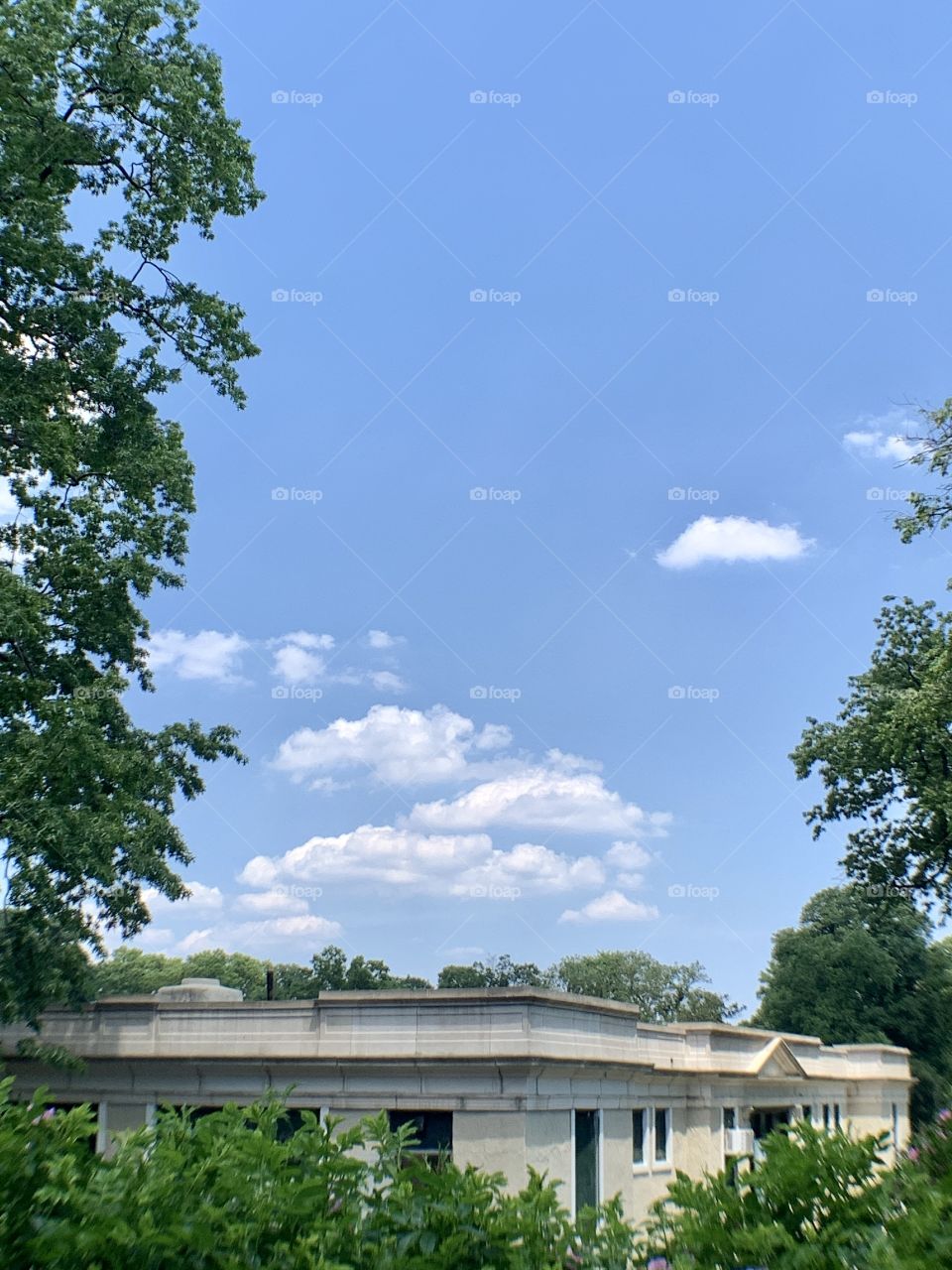 A sunny day, tennis court roof building in Central Park. Clouds and blue sky and trees.