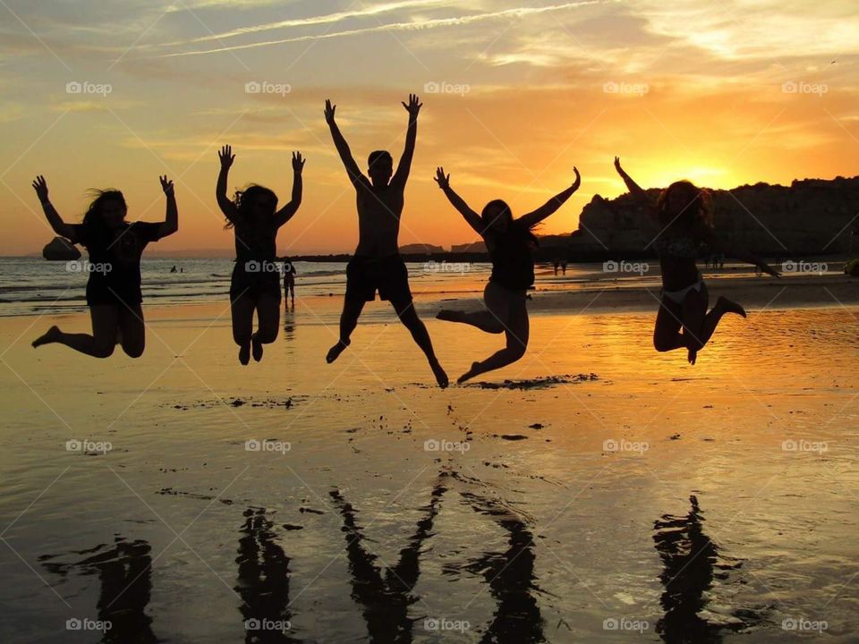 Shapes of five friends jumping on a sunset background 