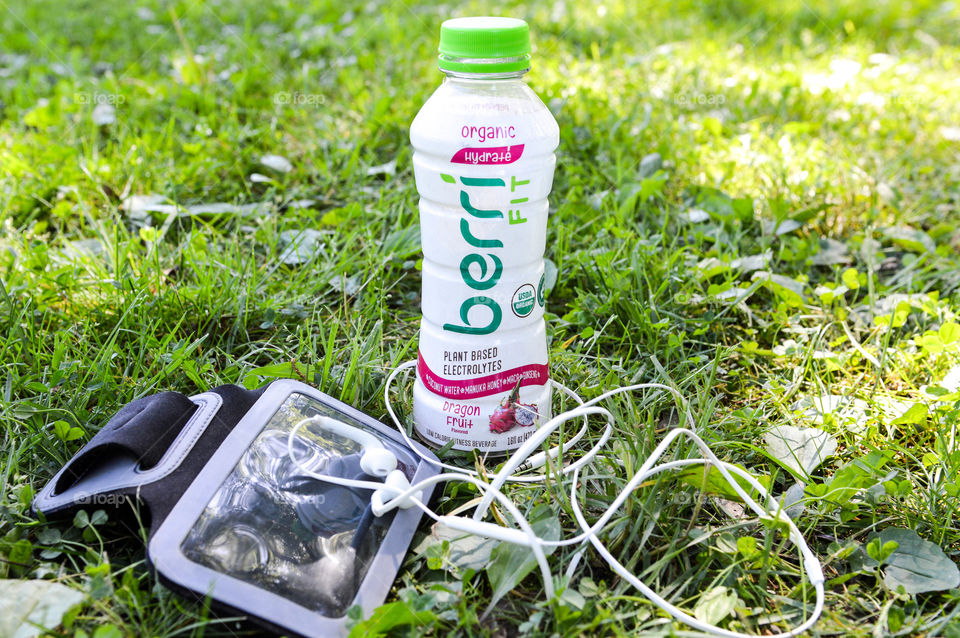 Bottle of Berri fit in the grass next to an arm band and headphones