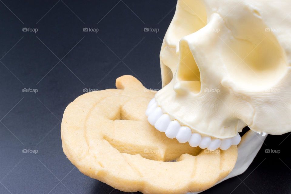 Skull biting a Halloween pumpkin-shaped cookie.