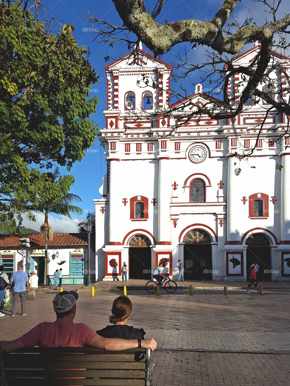 A couple enjoy looking at a church from a shady spot on the plaza in Guatape, Colombia.
