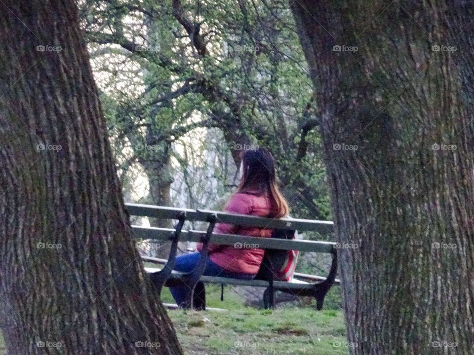 A woman sitting on the bench wearing a red coat 