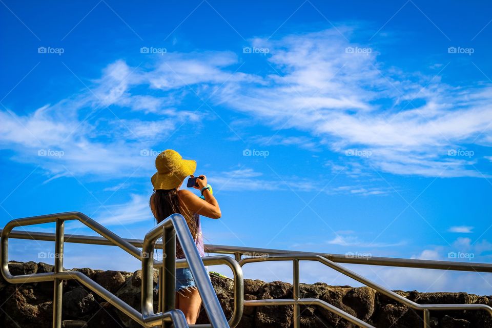 Picture of a woman in a straw hat taking a photo with a iPhone