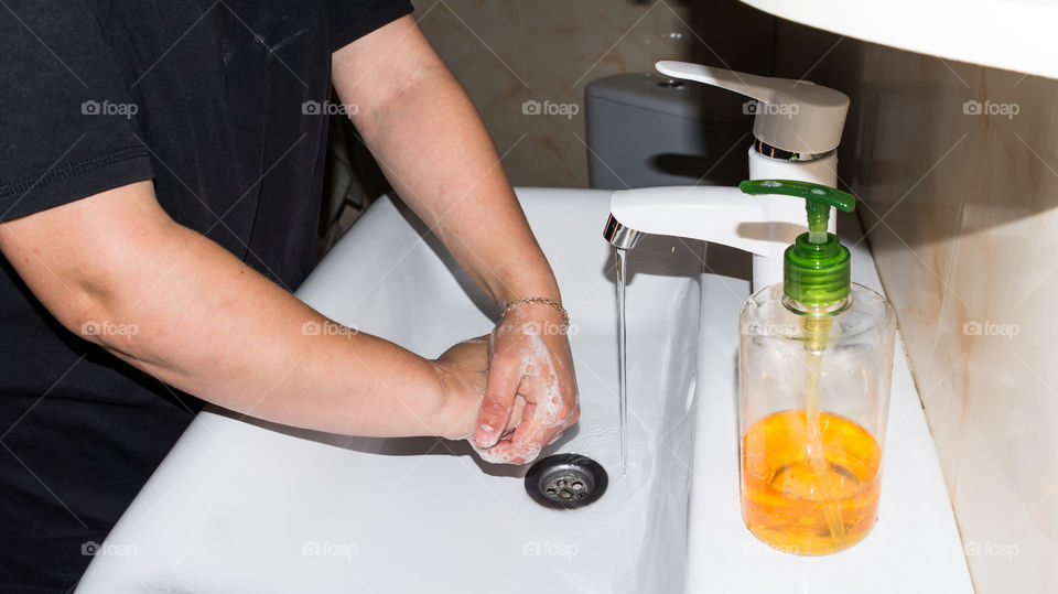 A man thoroughly washes his hands with soap in the bathroom, in a white washbasin with a white tap and antibacterial soap, makes a lot of foam and washes fingers and brushes after walking on the stree