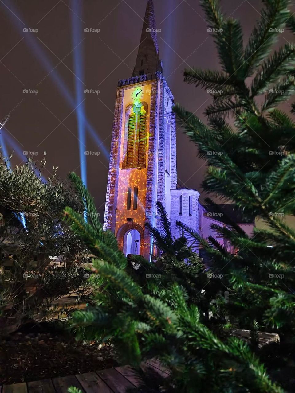 Light show on the parish Saint-Pierre & Saint-Paul of Quéven surrounded by fir trees at nightfall