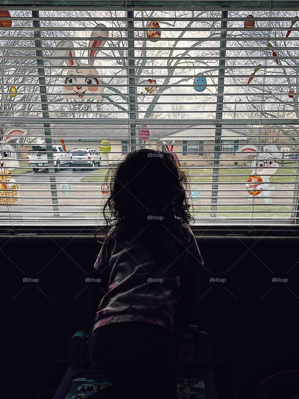 Toddler girl looks out window at neighborhood, neighborhood watch in full effect, little girl peers out of window, shadows to light, toddler in the shadows looking to the light, natural light portrait, toddler girl loves watching cars go by